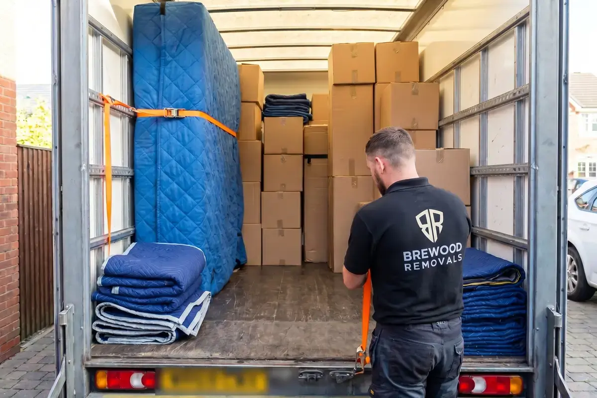 A Brewood Removals crew member strapping blanket-wrapped furniture securely inside a loaded van